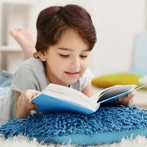 A young girl is lying on the floor, smiling, and reading a book.
