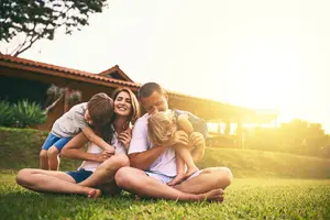 A family of four sitting on the grass in front of a house with a beautiful sunset