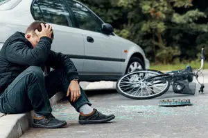 A man sitting on the sidewalk with his head in his hands after a bicycle accident