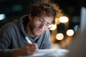 A man sitting and writing in a book with a laptop
