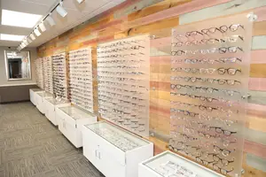 A display of glasses arranged on a wall with a wooden design, illuminated by ceiling lights, and a mirror on the left side.