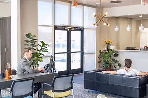 Two men sitting in an office one sitting at a desk and the other lounging on a couch