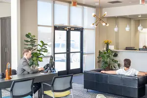 Two men sitting in an office one sitting at a desk and the other lounging on a couch