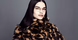 A woman with black hair wearing glasses and a leopard-print fur coat posing for a photo