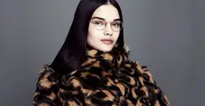 A woman with black hair wearing glasses and a leopard-print fur coat posing for a photo