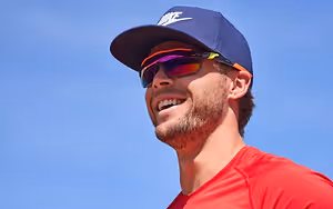 A man wearing a red shirt and a blue Nike hat with sunglasses
