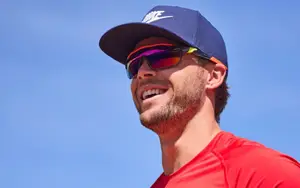 A man wearing a red shirt and a blue Nike hat with sunglasses