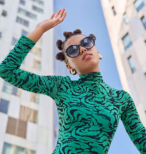 A woman wearing a green long-sleeve dress with a swirl pattern poses in front of a building.
