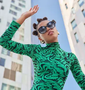 A woman wearing a green long-sleeve dress with a swirl pattern poses in front of a building.