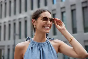 Close up of woman wearing a blue dress and gold sunglasses smiling at the camera