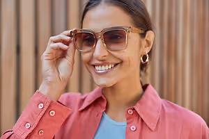 A woman is adjusting her glasses while smiling and posing for a photo in a wooden room
