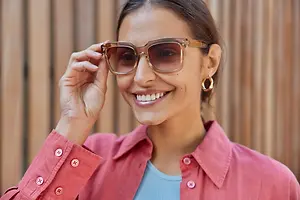 A woman is adjusting her glasses while smiling and posing for a photo in a wooden room