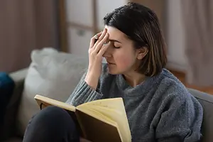 Woman reading a book while rubbing her temple