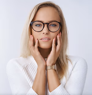 A blonde woman wearing glasses and a white sweater with her hands on her cheeks