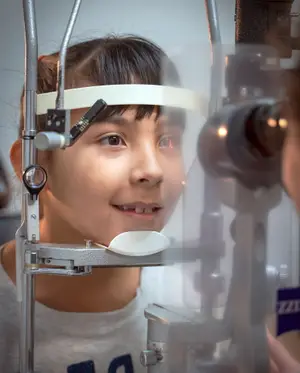 A girl is getting her eye examined by an optometrist using a slit lamp.