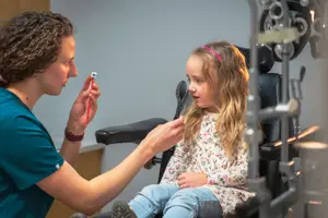 An optometrist is examining the eye of a young girl