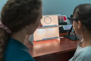 Two girls are looking at a blueprint through a light box on a table.