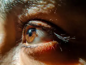 A close-up of a human eye with long eyelashes and a reflection of light on the iris.