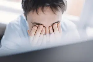 A man covering his eyes with his hands in front of a computer