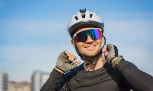 A man in cycling gear is adjusting his helmet and goggles while smiling