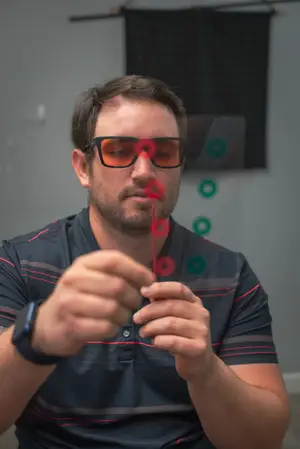 A man wearing orange glasses and holding a red string while looking at something in front of him