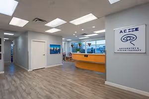 Absee Optometry and Vision Therapy's reception area features a wooden counter, gray walls, and a sign with an eye icon, surrounded by a serene and welcoming atmosphere.