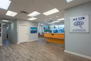 Absee Optometry and Vision Therapy's reception area features a wooden counter, gray walls, and a sign with an eye icon, surrounded by a serene and welcoming atmosphere.