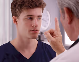 A male doctor points to a teenage boy's ear as he examines it.
