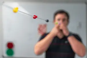 A man playing a toy instrument by blowing through a pipe with colored beads.