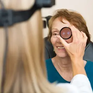 An older woman is having her eyes examined by an optometrist with a magnifying lens