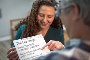 A woman holding a piece of paper with text about bees and butterflies points at it while smiling, a man is looking at her smiling as well