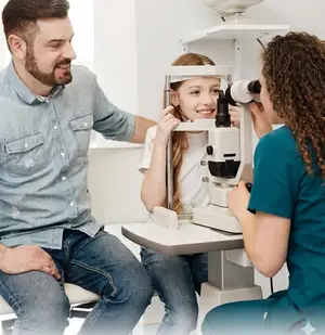 A man and a woman are looking at a girl's eyes using a microscope in a medical room.