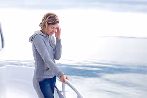 A woman holding her head to soothe a headache standing on a boat looking out at the ocean