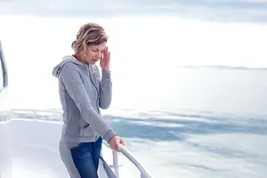 A woman holding her head to soothe a headache standing on a boat looking out at the ocean