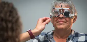 An older woman is adjusting her glasses with the help of a young woman in front of her.