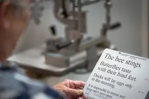 An elderly man wearing glasses is reading a piece of paper with text about nature, with a blurry machine behind him.