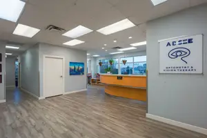 An image of an optometrist's office with a desk and a sign, and a picture hanging on the wall.