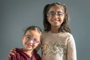 Two girls wearing glasses standing close to each other and smiling
