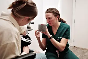 A woman in green scrubs shows a baby a piece of paper in a hospital room.