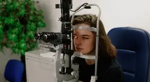 A woman is sitting and looking at a machine used for eye examination.