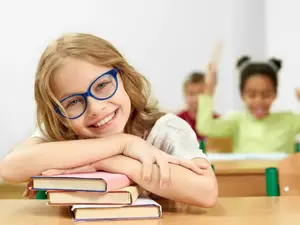 A girl sitting on a desk in a classroom, smiling and posing for a photo