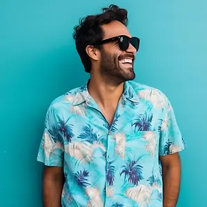 A smiling man with a beard wearing a blue tropical shirt and sunglasses standing in front of a blue background