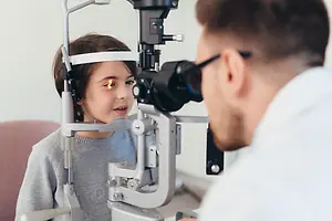 An ophthalmologist examining a young girl's eyes using a slit lamp.