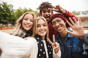 Group of young people smiling and making peace signs with their fingers in an outdoor area