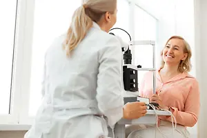 An optometrist is examining a patient's eye with an ophthalmoscope in an optical clinic