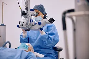 A woman doctor is sitting and looking through a microscope in an operating room