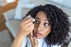 A woman with curly hair is putting eye drops in her eye.