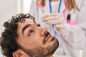 A male patient with a beard and mustache is getting his nose swabbed for a test in a medical setting.