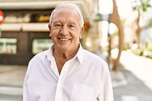 Senior man in a white shirt smiling on a sidewalk