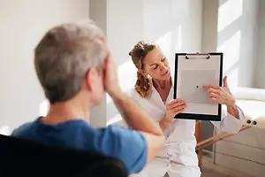 A man is seated and appears to be undergoing an eye examination conducted by a woman wearing a white robe.